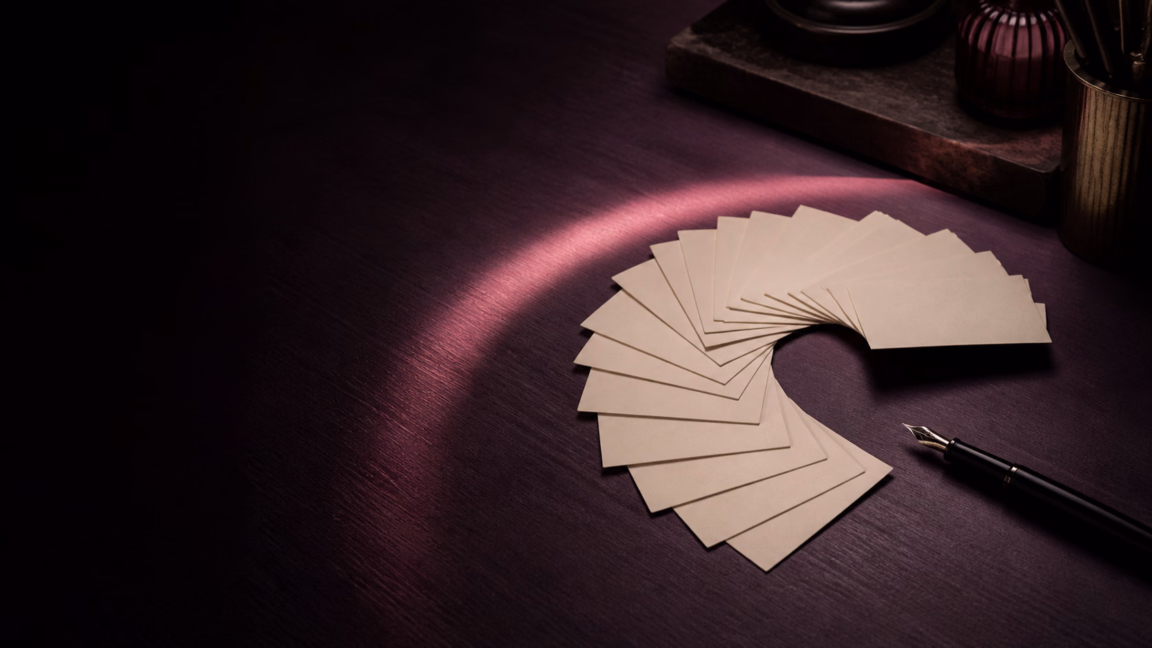 Cream note cards arranged in a loose spiral beside a fountain pen on a dark plum desk.